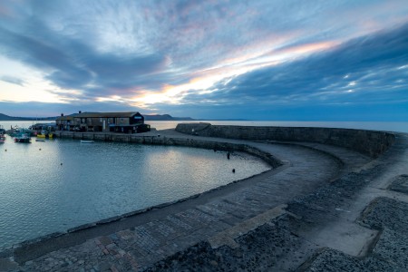 The Cobb with dramatic sky and harbour buildings